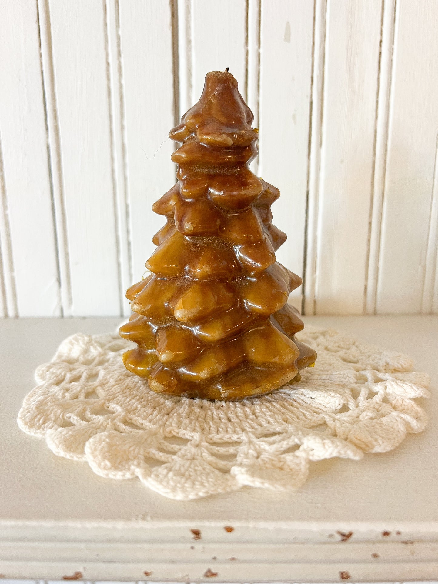 vintage honey-colored Christmas tree candle sitting on cream crochet doily against white beadboard wall