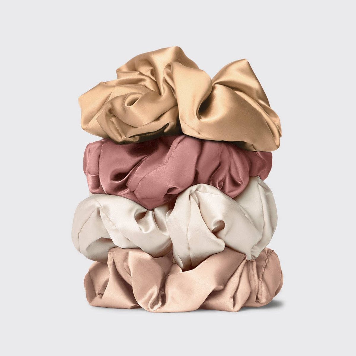 Stack of beige, pink, and white satin pillow scrunchies on a light gray background