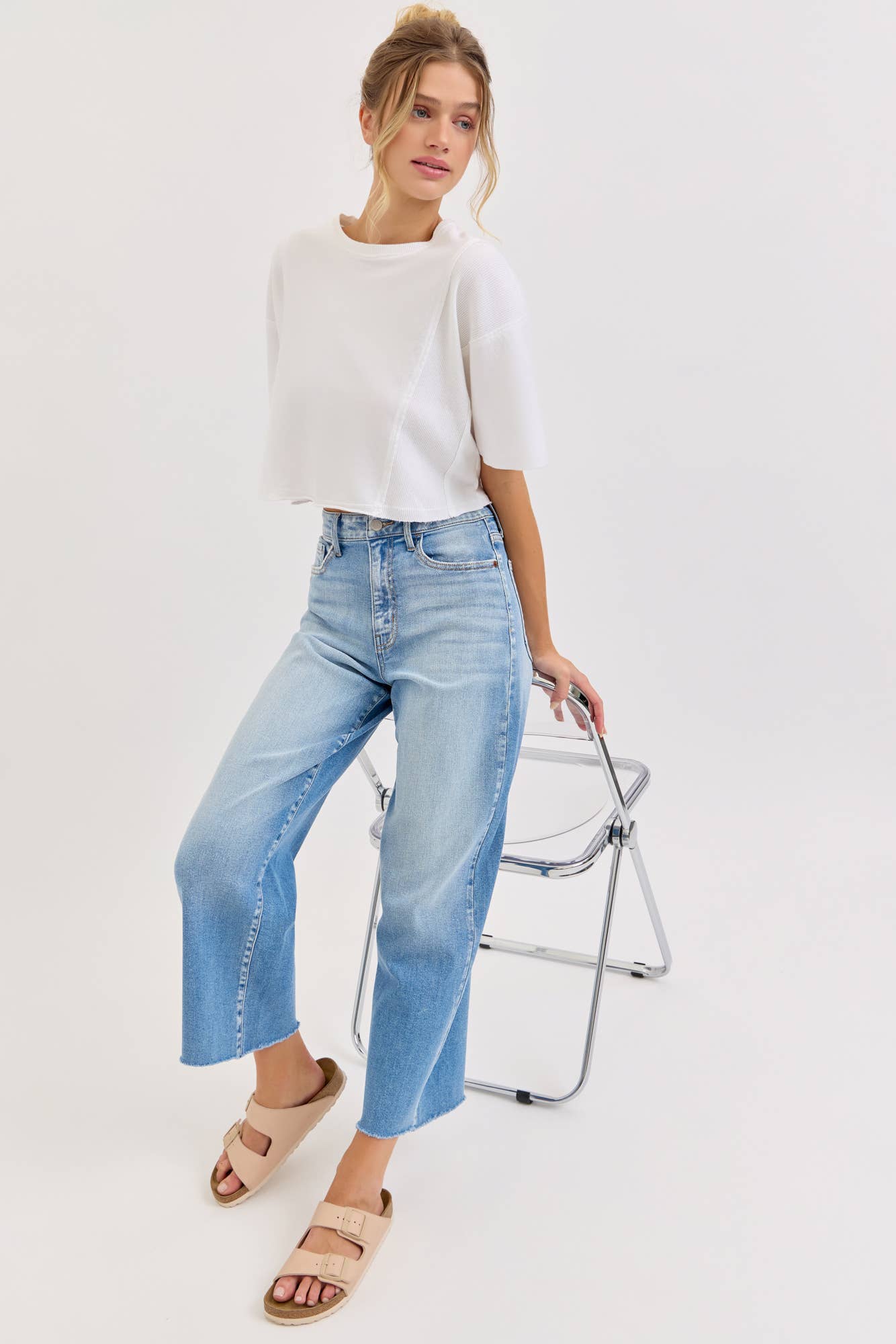 Woman wearing a white top and light blue jeans standing against a white background