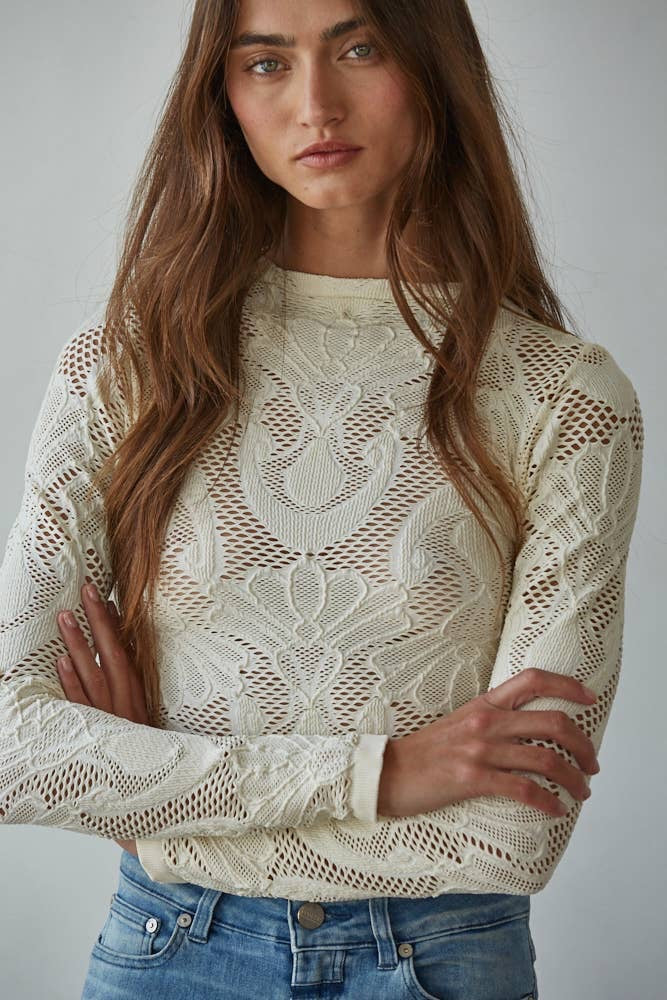 Close-up detail of cream floral lace fabric on fitted long sleeve top