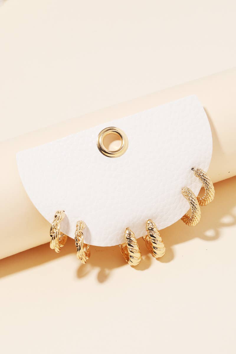 Gold textured mini hoop earring trio displayed on a white leather card against a creamy neutral background — elegant, minimal, boutique jewelry.