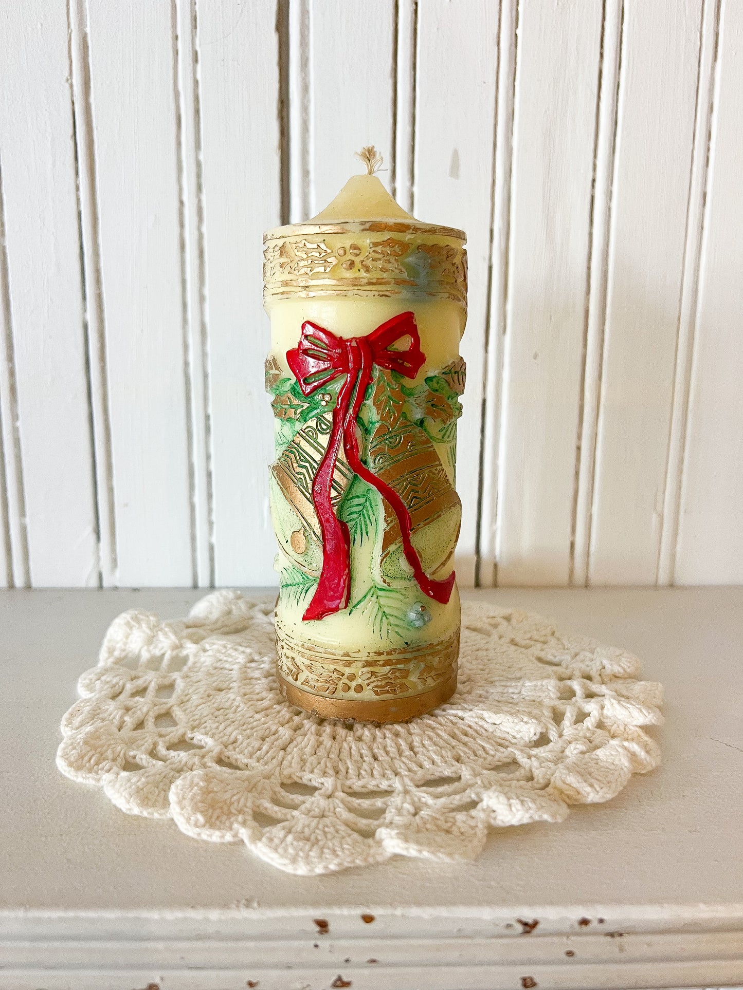 vintage pillar candle with embossed gold details and red ribbon bow featuring Christmas bells design on crochet doily