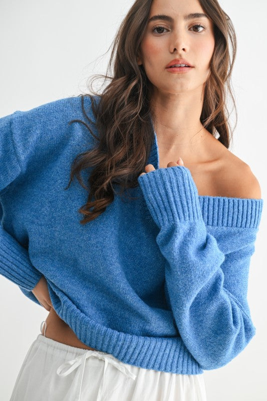 Woman wearing a relaxed cornflower blue V-neck sweater tucked into a white tiered skirt, standing against a plain white background.