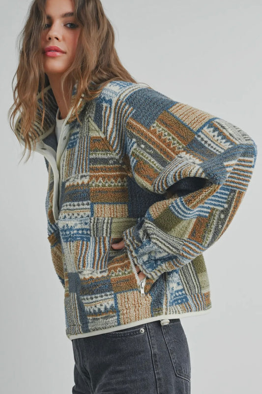 Woman wearing a vintage-inspired patchwork sherpa pullover in blue, olive, rust, and cream tones. The cozy half-zip fleece has a relaxed fit and textured boho design.