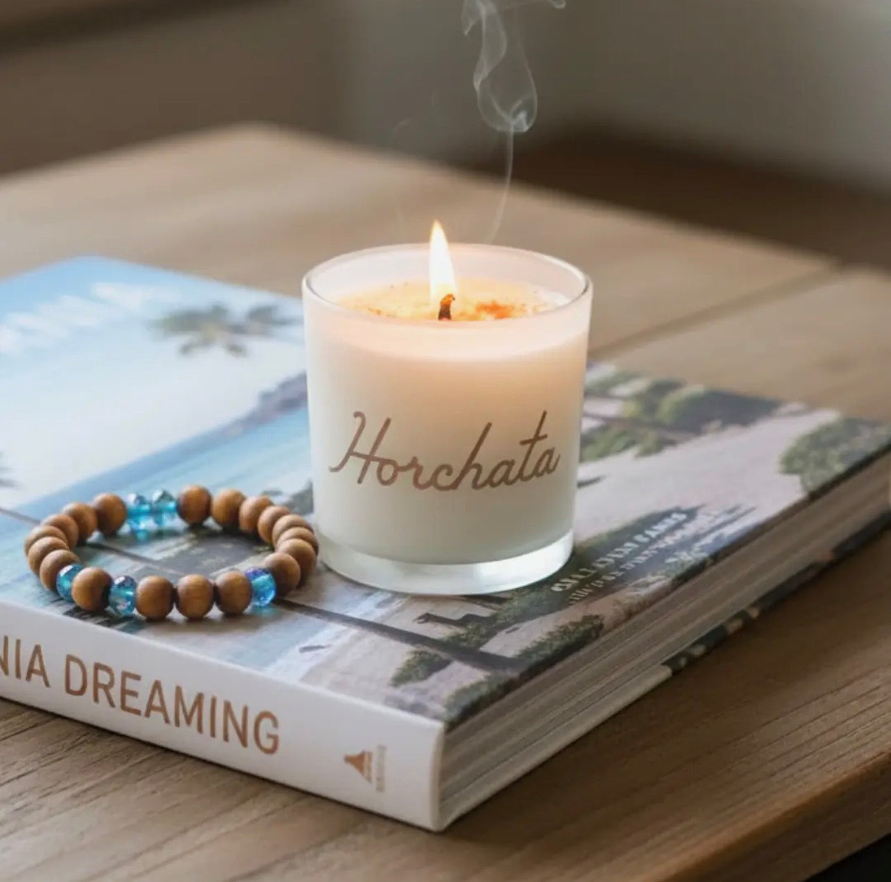 Candle labeled 'Horchata' on a book with a wooden beaded bracelet