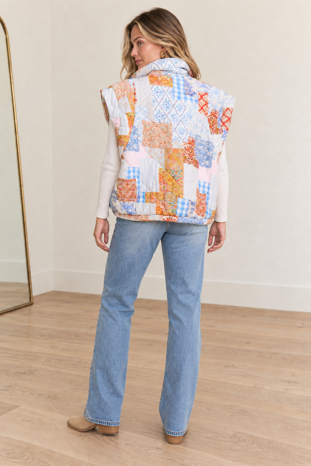 Back view of women’s oversized patchwork quilted vest styled with a cream long sleeve and relaxed jeans