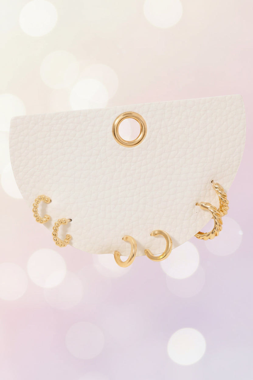 Three-pair dainty gold mini hoop earring set on a white card against a soft dreamy background, featuring beaded, smooth, and twisted textures — minimal, feminine boutique jewelry.