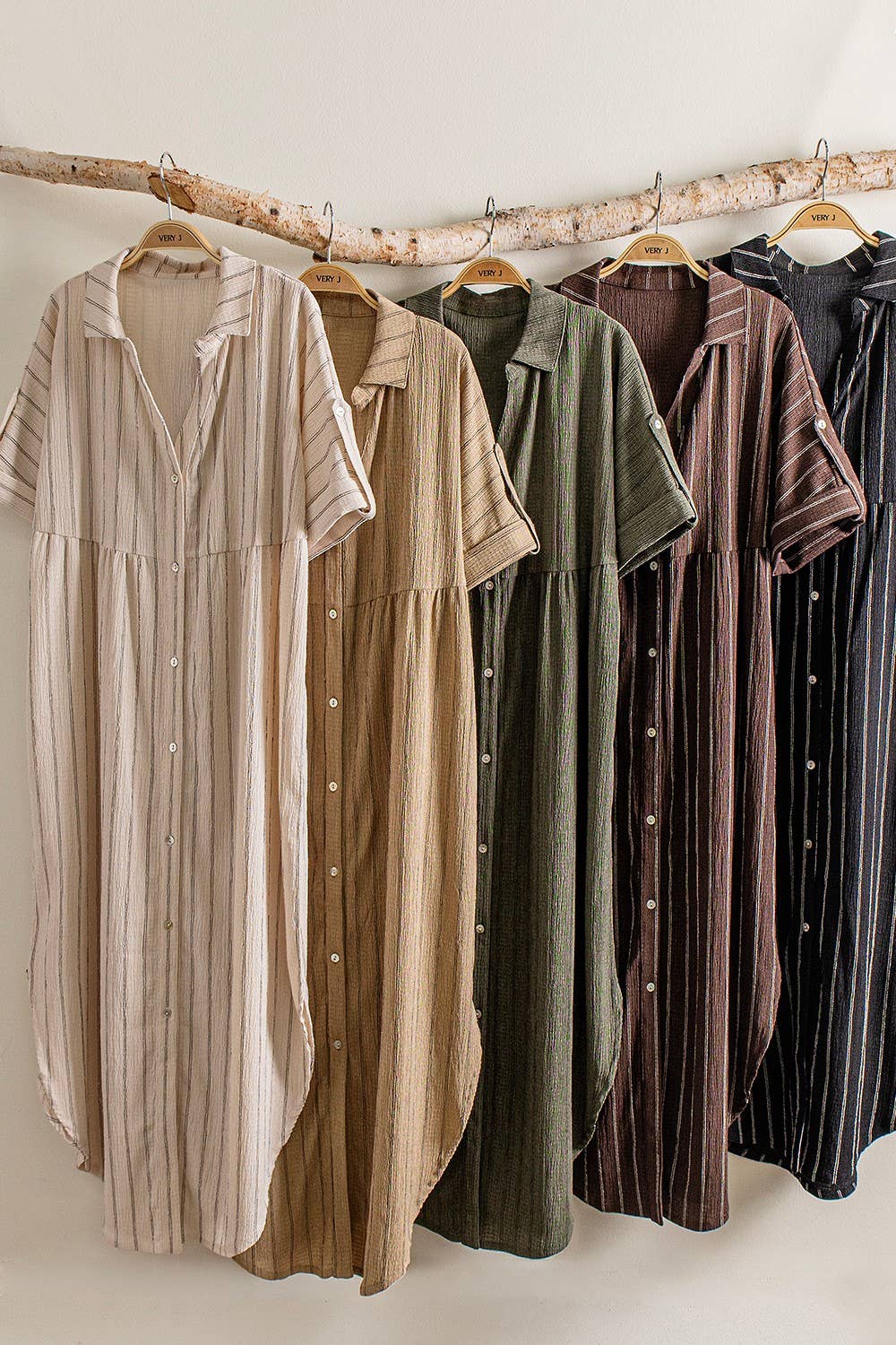 Row of dresses in various colors hanging on a wooden rack against a white wall.
