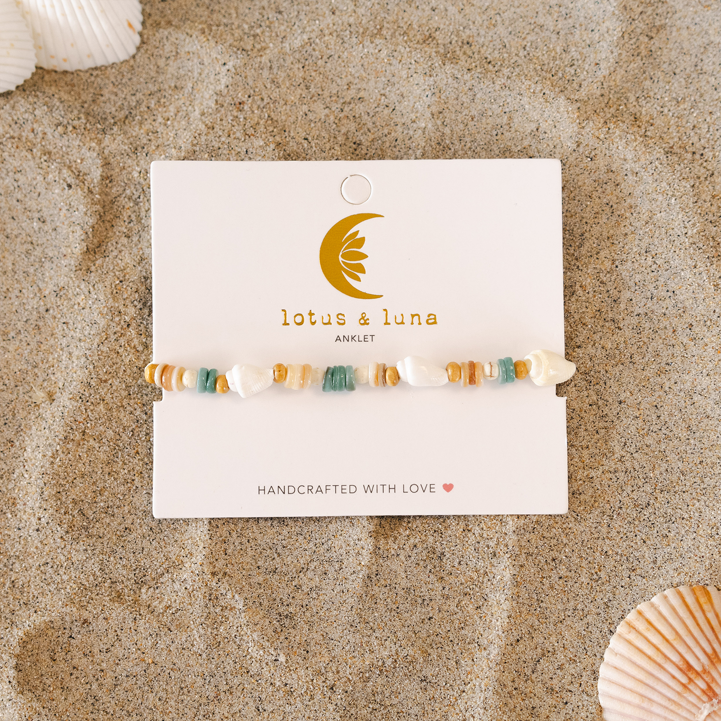Beaded bracelet on a 'lotus & luna' card with seashells on sand