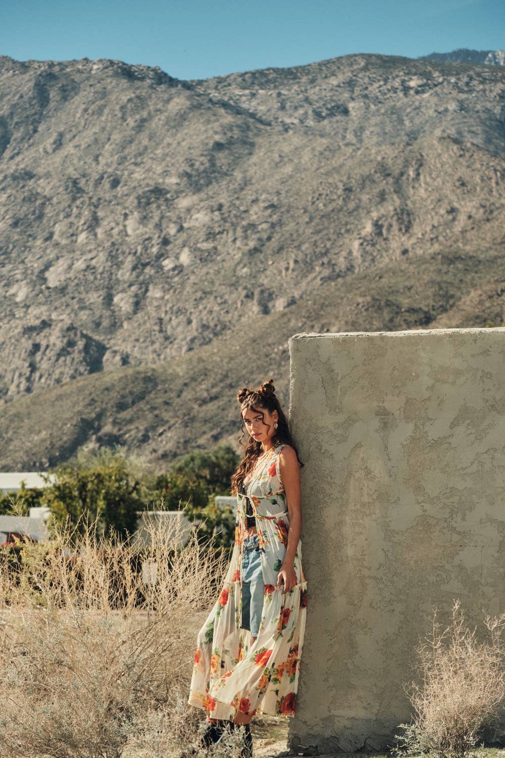 Woman in a floral dress standing against a stone wall with mountains in the background