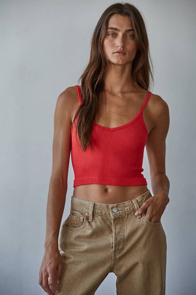Woman wearing a red ribbed tank top and beige pants against a plain background