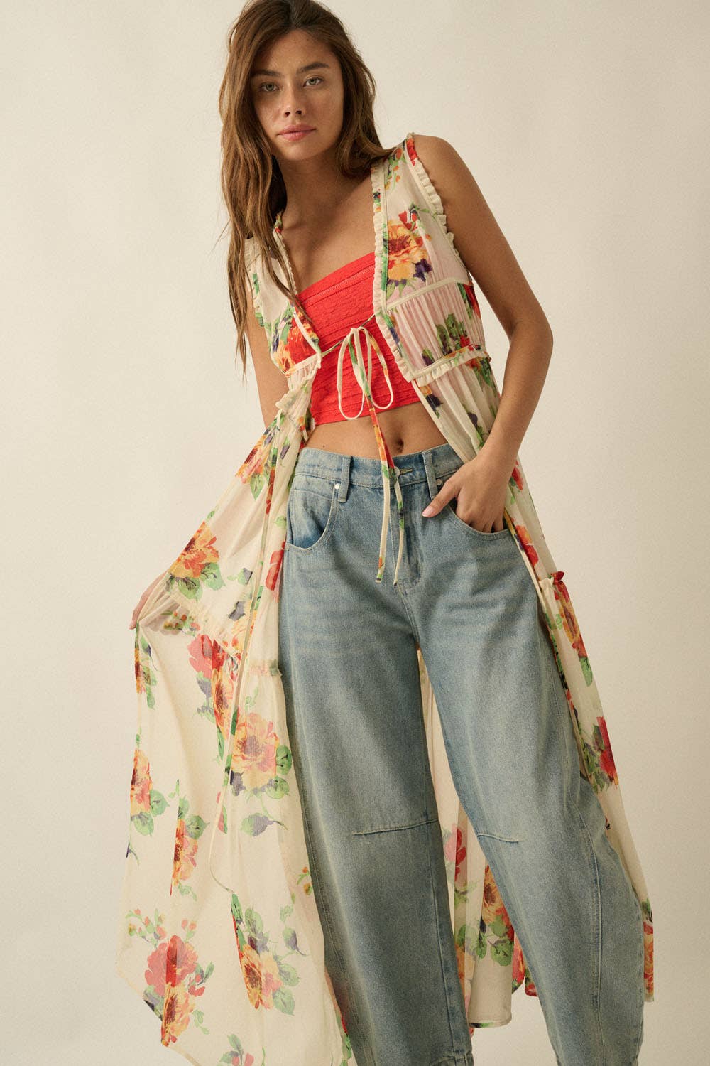 Woman wearing a floral kimono over a red top and blue jeans on a plain background