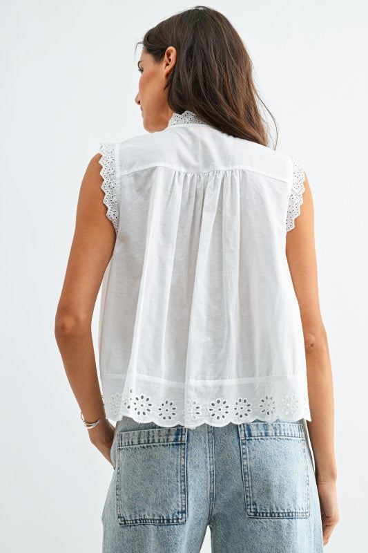 Woman wearing a white sleeveless top with lace details on a plain background