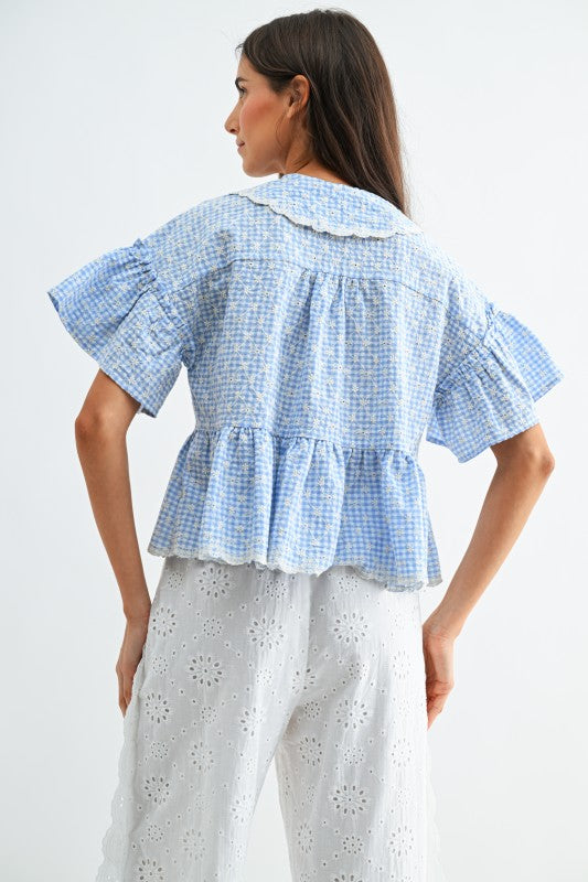 Woman wearing a blue checkered blouse with ruffled details on a white background