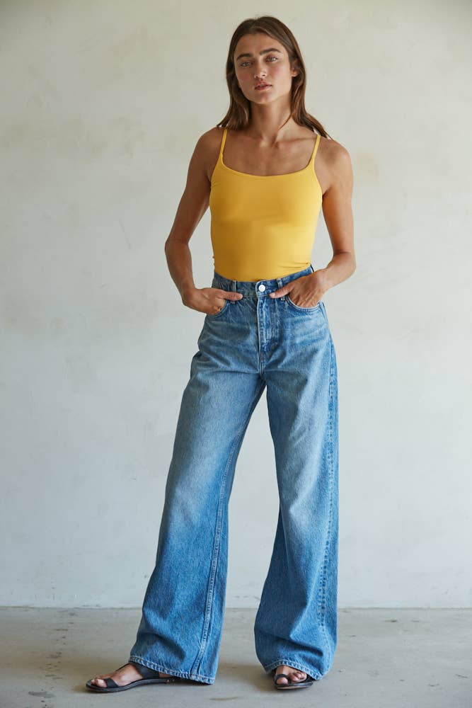 Woman wearing a yellow tank top and blue jeans against a plain background