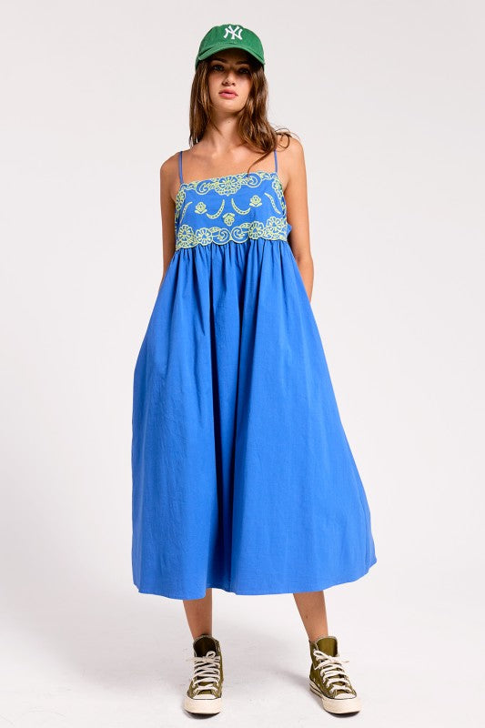 Woman wearing a blue dress with floral lace details and a green cap on a white background