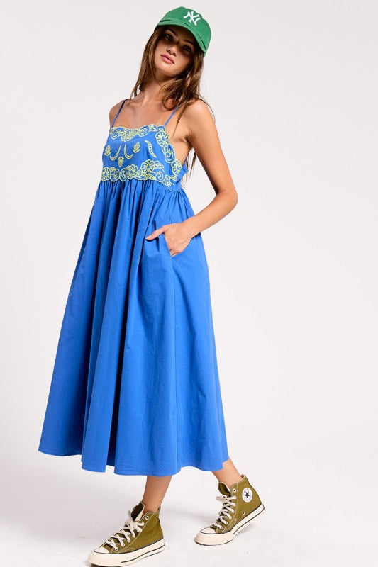 Woman wearing a blue dress with floral embroidery and green sneakers on a white background