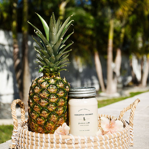 Pineapple Coconut soy candle beside whole pineapple in woven basket for beach inspired summer decor.
