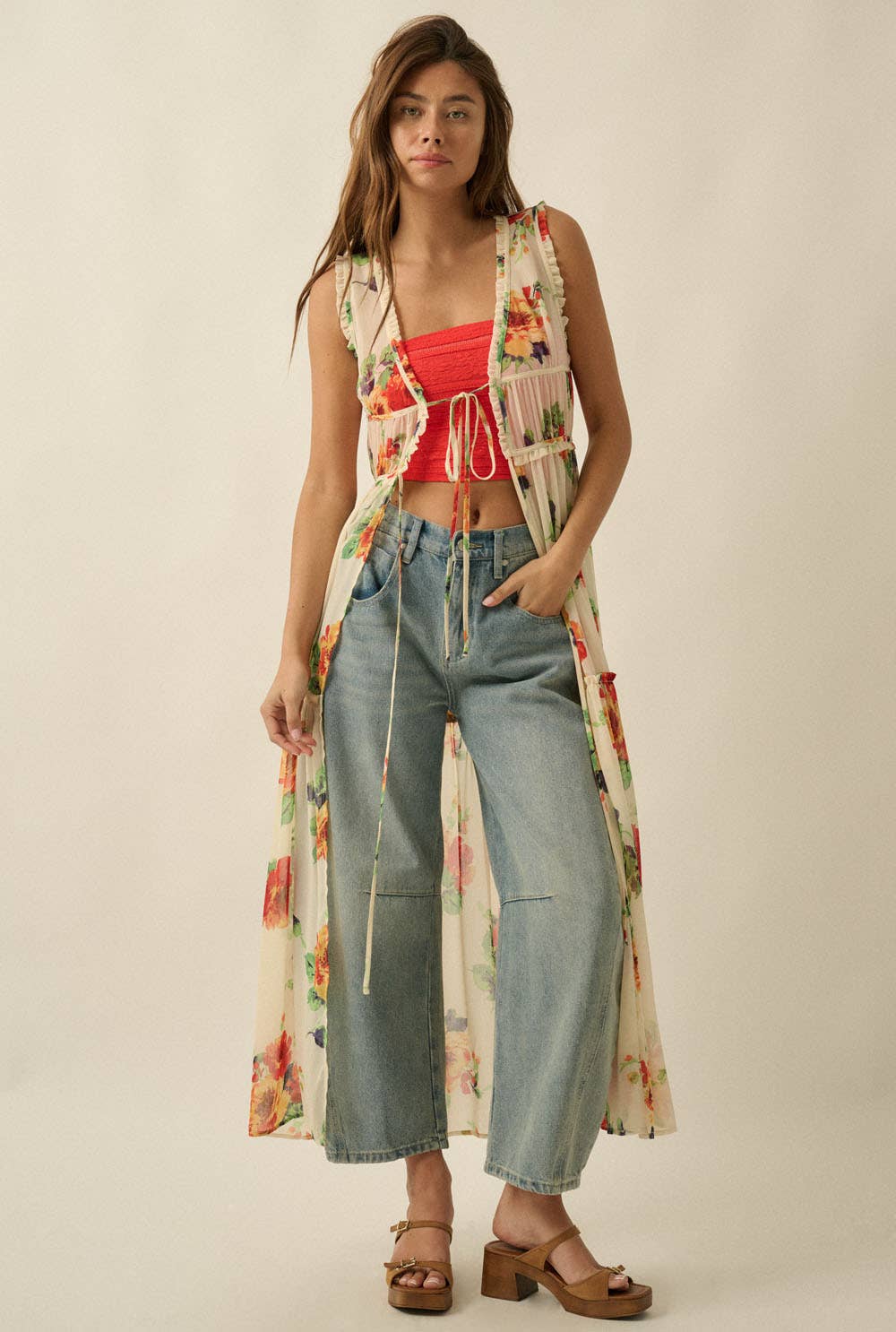 Woman wearing a sheer vintage floral maxi duster with front tie closures layered over wide-leg denim jeans and a bright coral bandeau top.