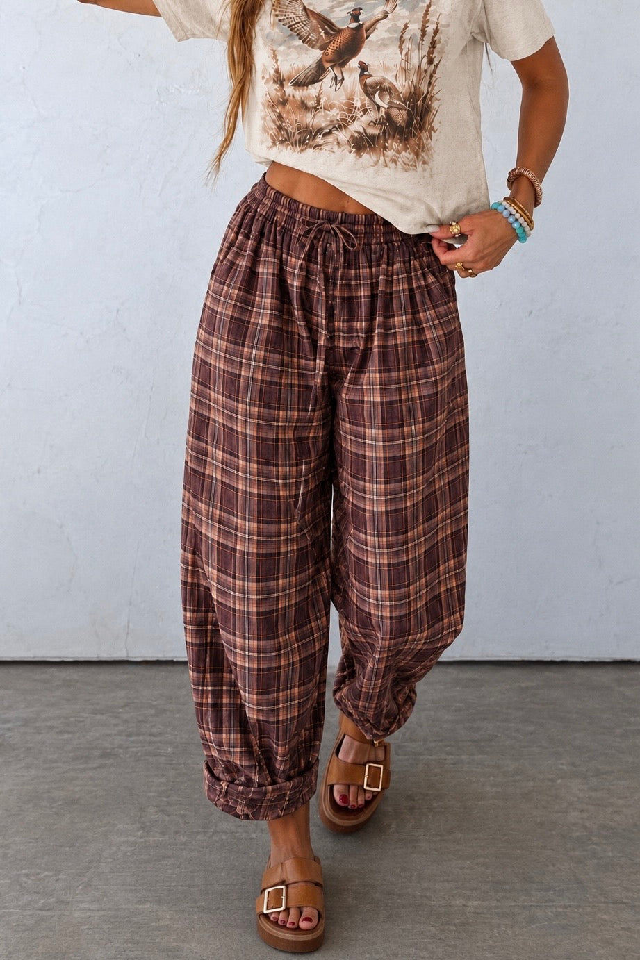 Woman wearing brown and berry plaid balloon pants with a vintage pheasant graphic tee and brown buckle sandals.