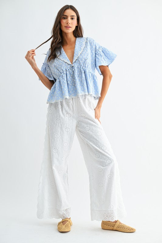 Woman wearing a blue and white checkered top and white pants on a white background