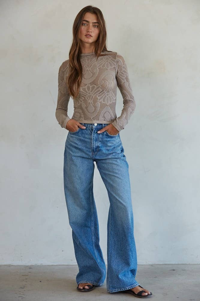 Woman wearing a mauve floral lace long sleeve top styled with high-waisted denim jeans
