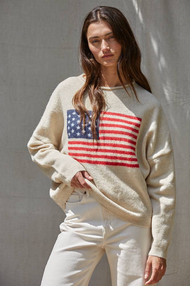 Cream knit sweater featuring a large American flag jacquard design on the front with a relaxed fit and long sleeves.
