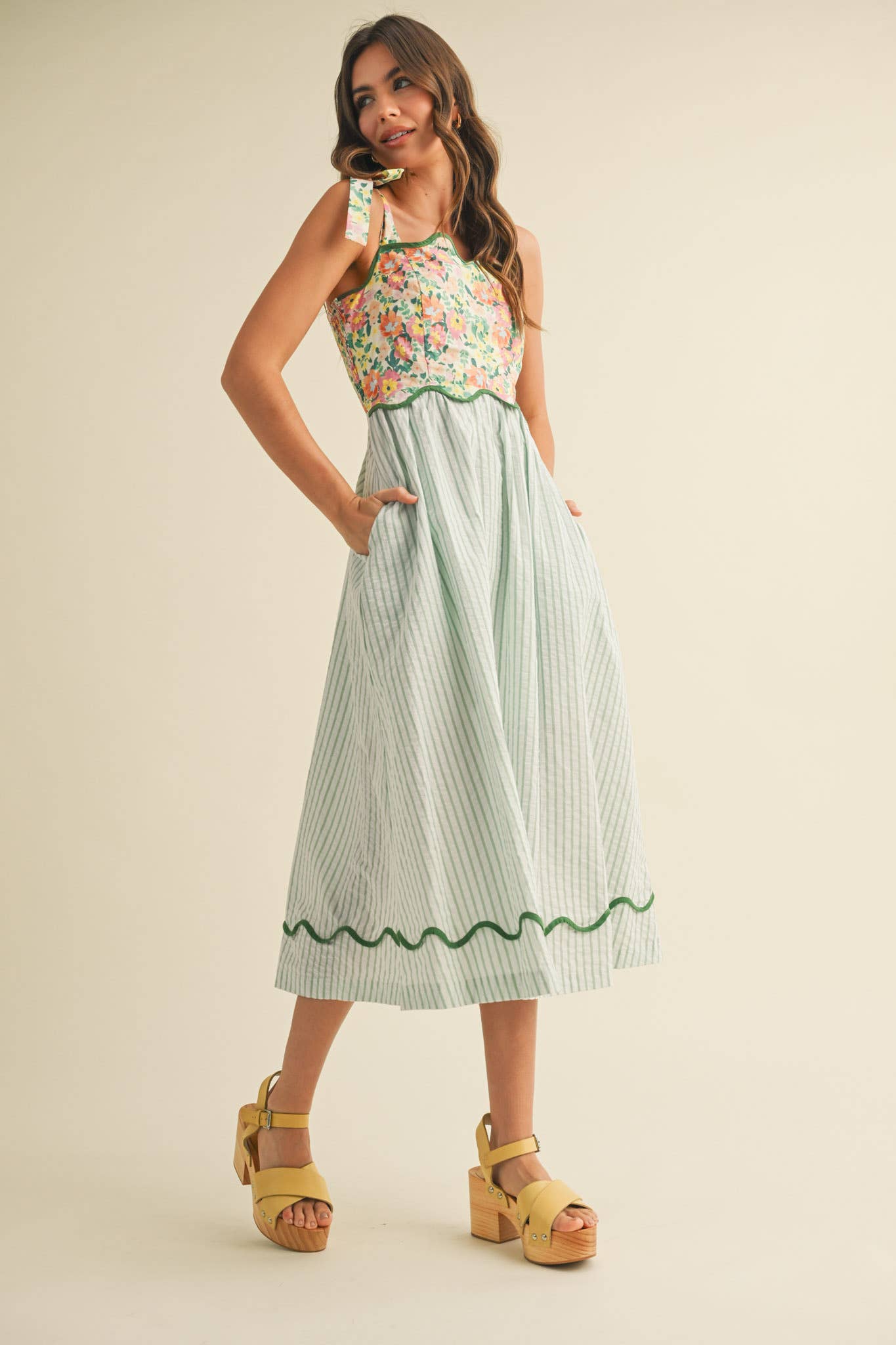 Woman wearing a floral top and striped skirt with yellow shoes on a beige background