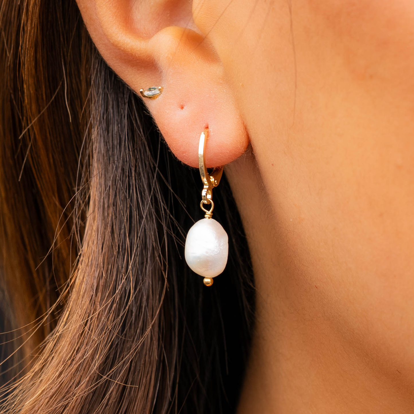 Pearl earring worn by a person with brown hair.