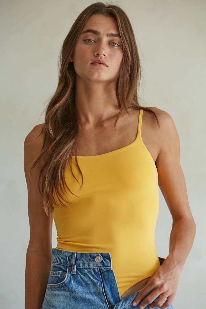 Woman wearing a marigold yellow seamless square neck bodysuit with adjustable straps paired with light wash wide-leg jeans.