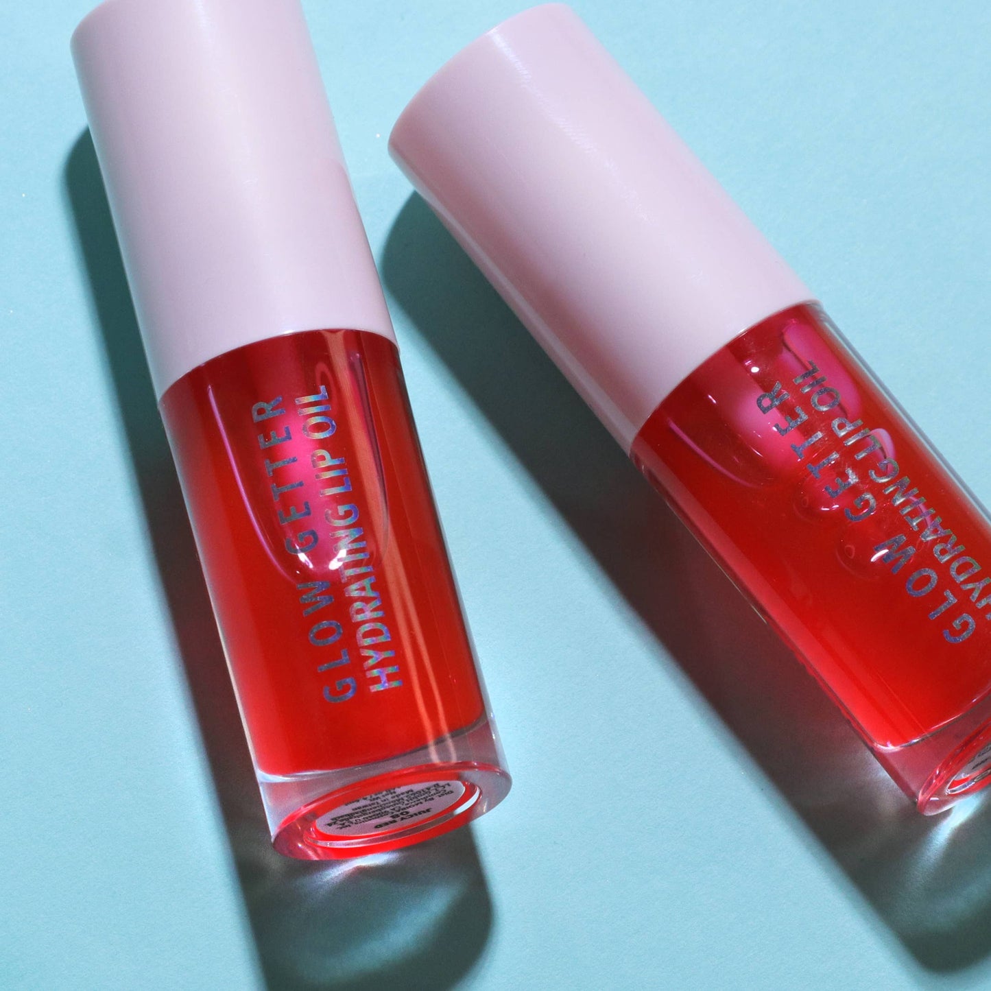 Two red lip gloss tubes with pink caps on a light blue background