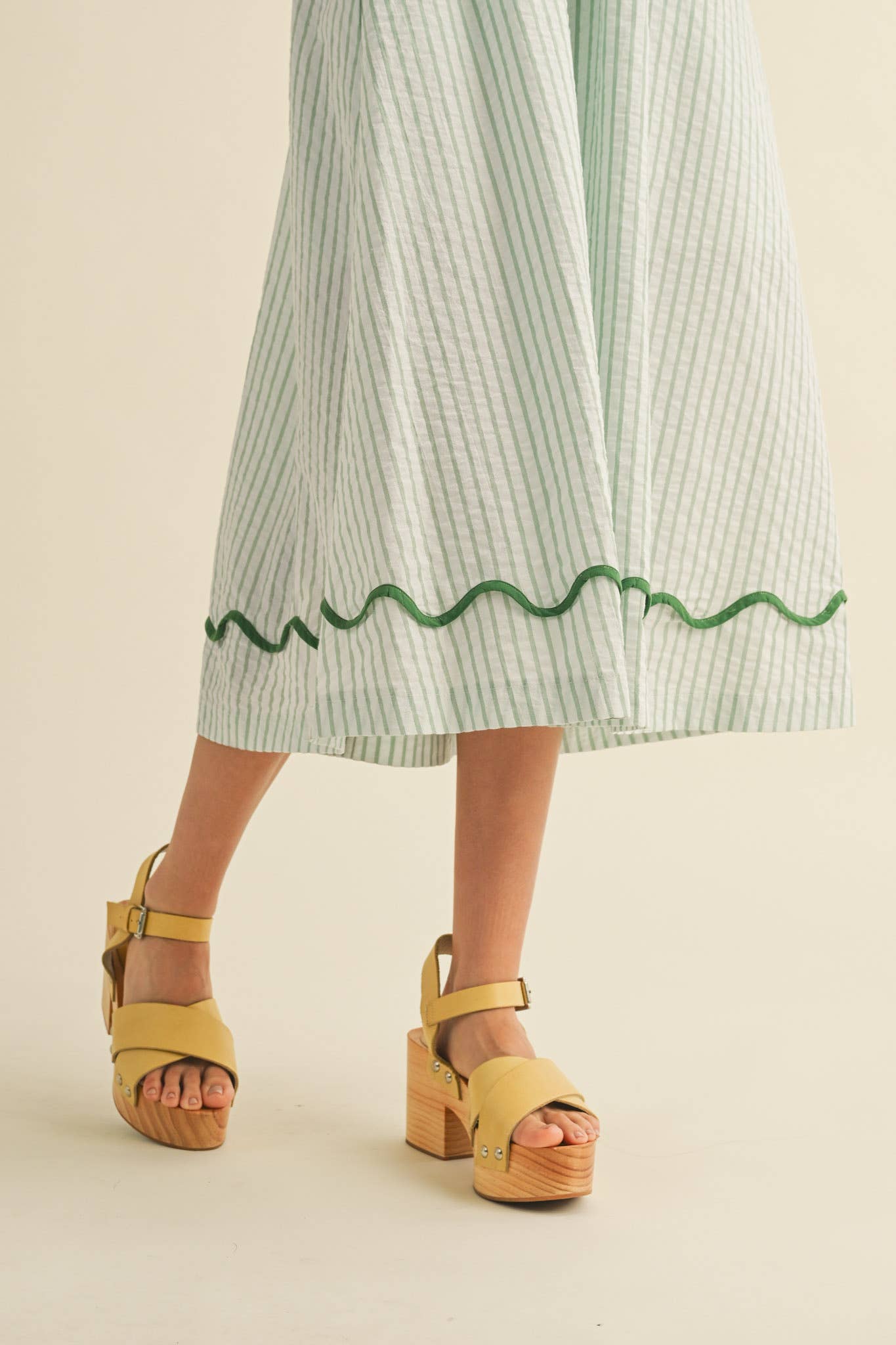 Person wearing a green dress with white stripes and yellow sandals on a beige background