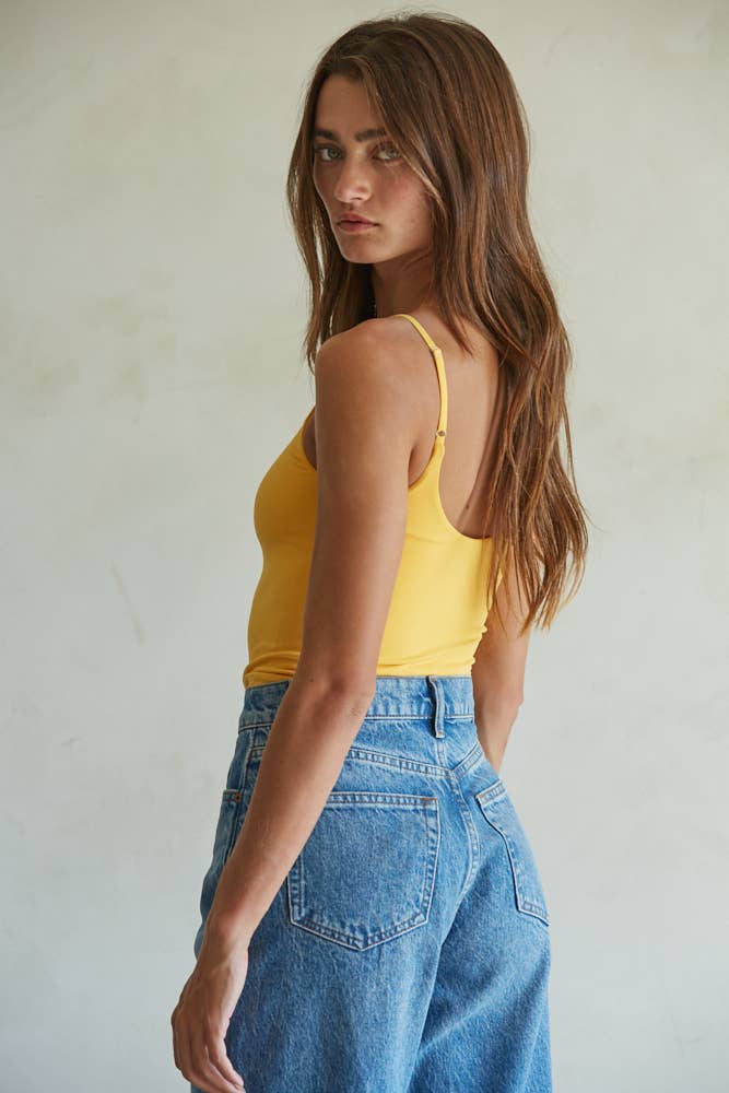 Woman wearing a yellow tank top and blue jeans against a plain background