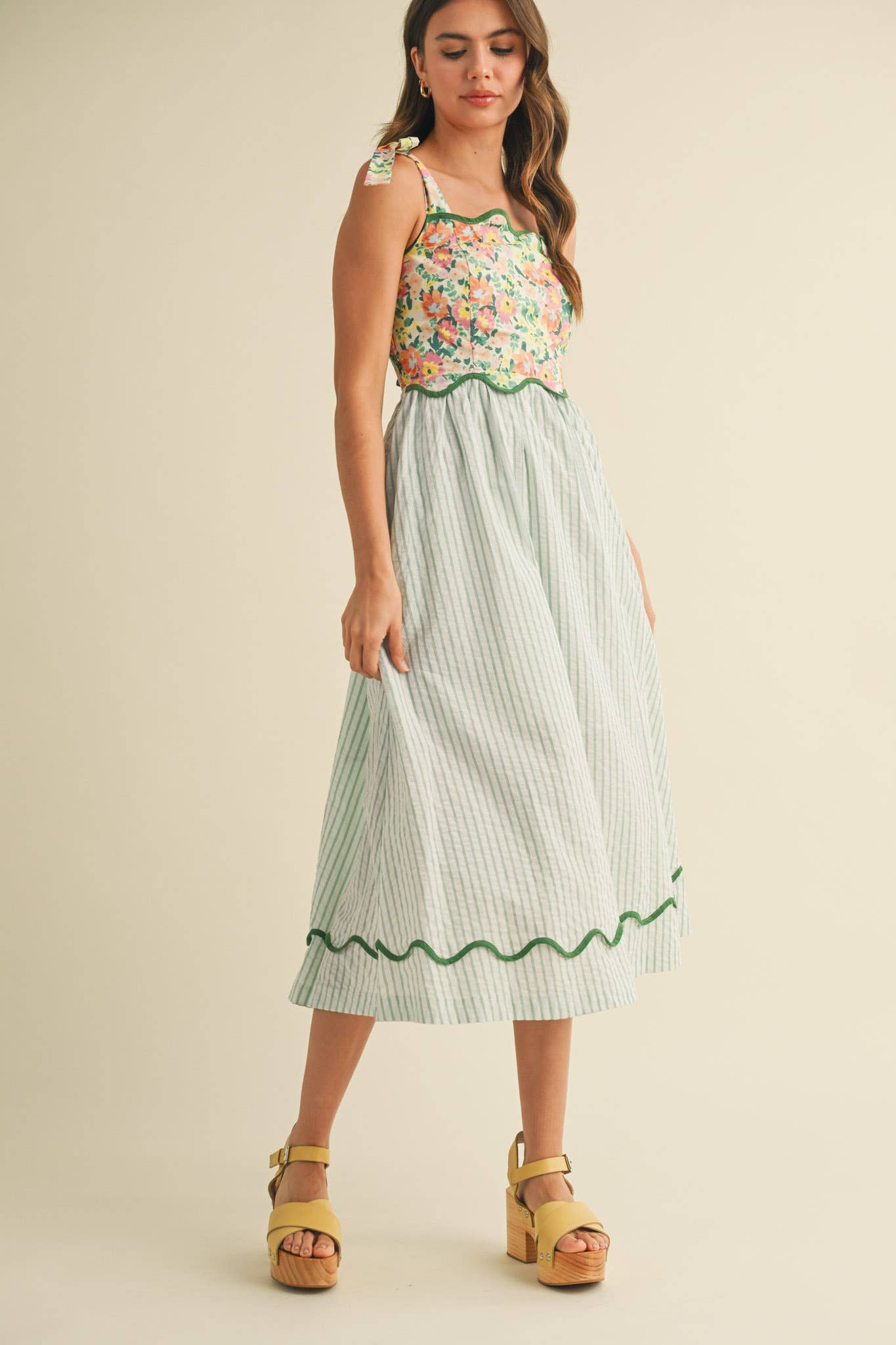 Woman wearing a floral top and green and white striped skirt on a beige background
