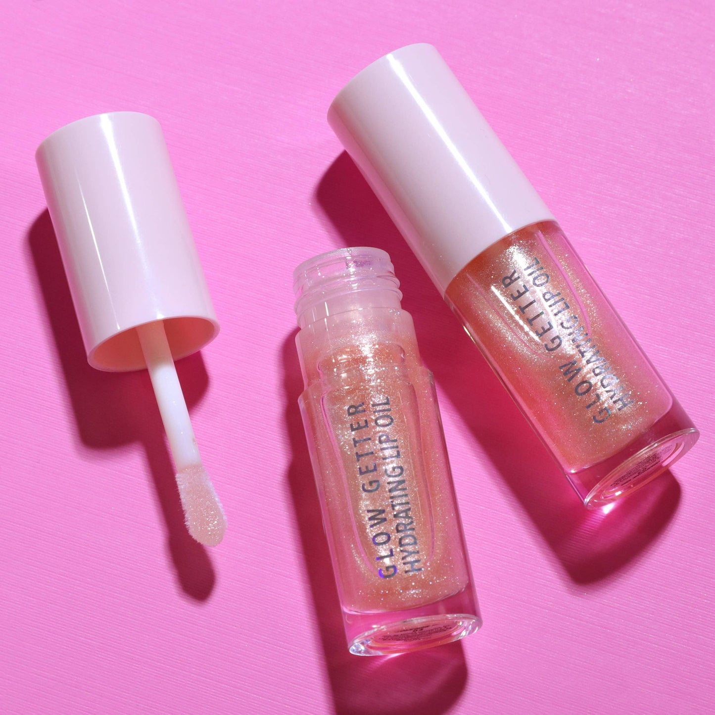 Two lip oil products with applicator on a pink background