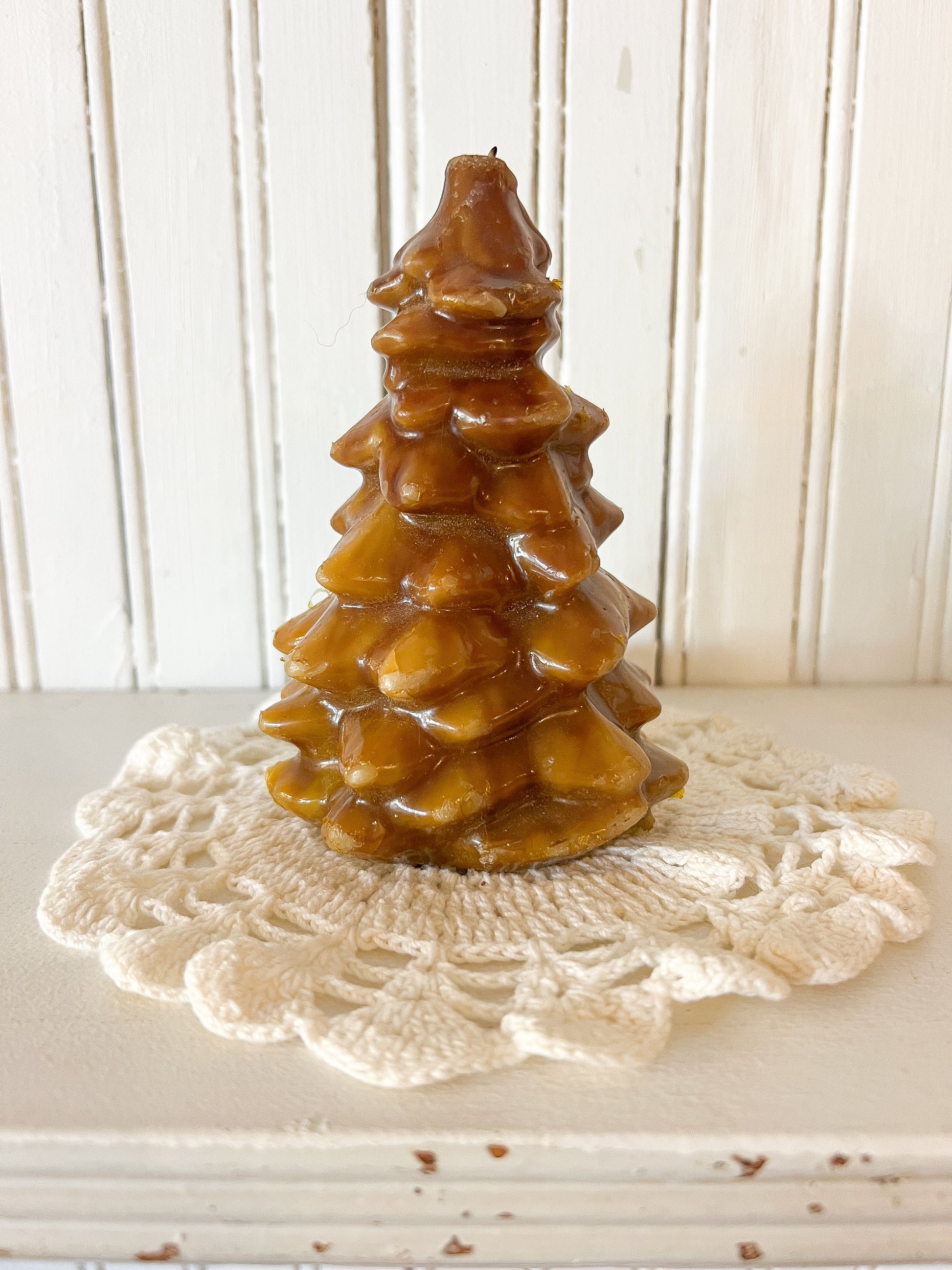 vintage honey-colored Christmas tree candle sitting on cream crochet doily against white beadboard wall