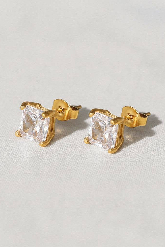 Square-cut clear stone stud earrings in a gold-tone setting, shown on an ear and as a pair on a light background.