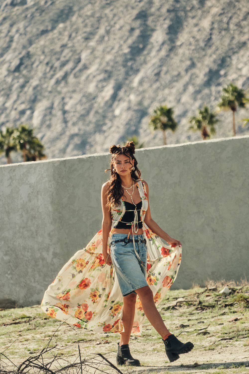 Woman in a floral dress and denim skirt standing against a mountainous background