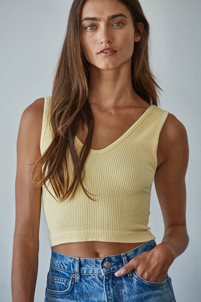 Woman wearing a yellow ribbed tank top and blue jeans against a plain background