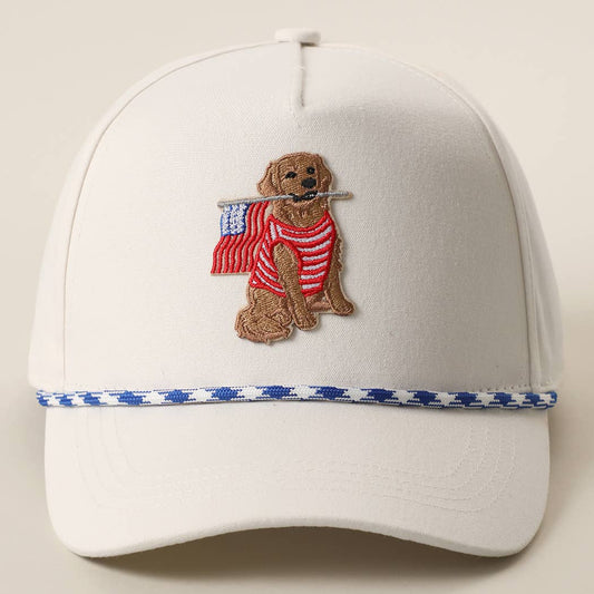 White trucker hat featuring an embroidered Golden Retriever wearing a striped shirt and carrying an American flag with a blue rope accent across the brim.