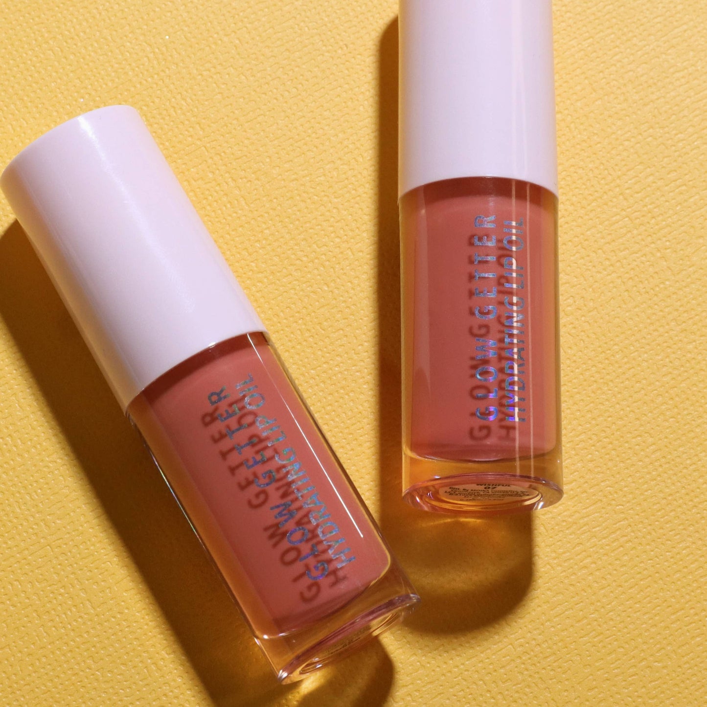 Two lip gloss products with white caps on a yellow background