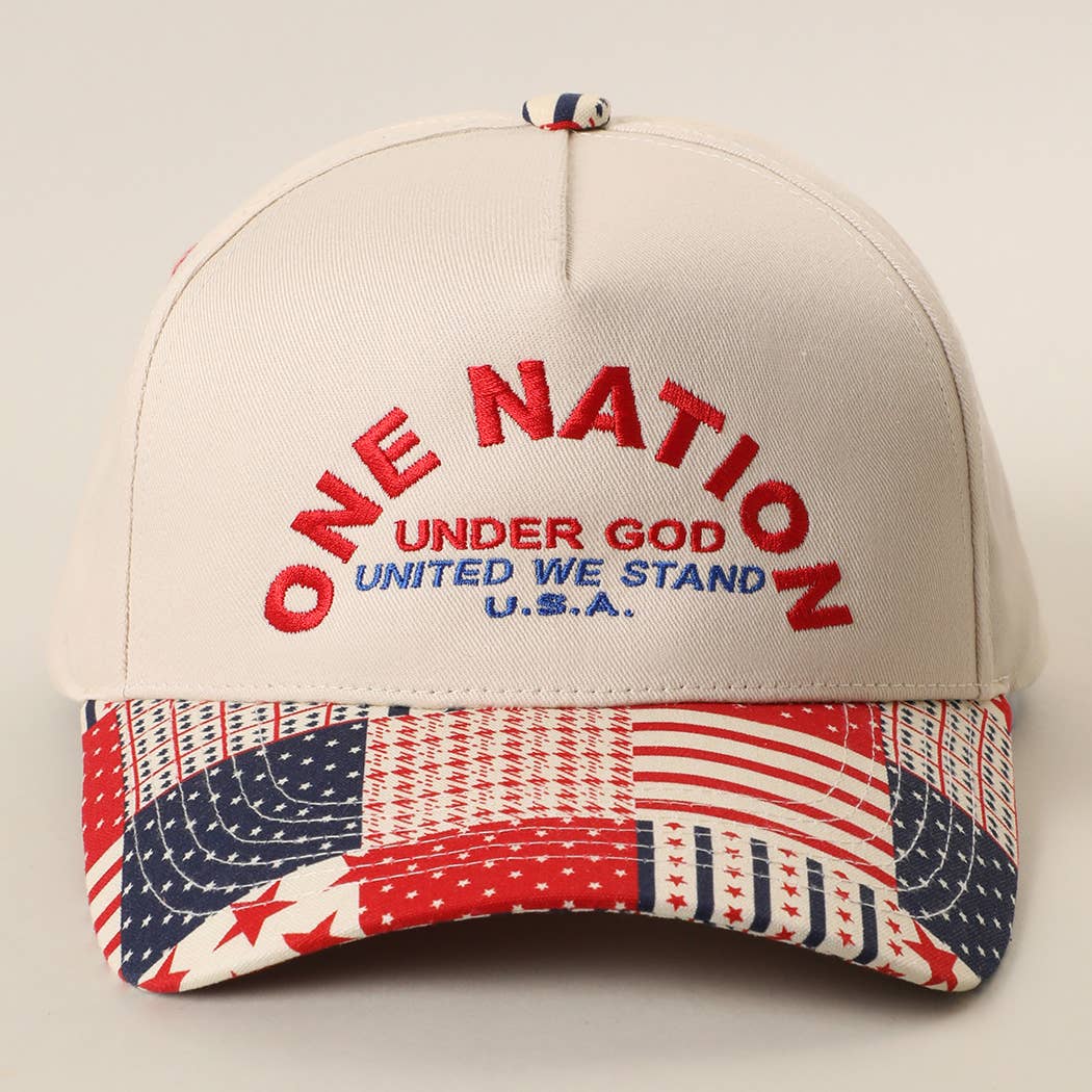 Ivory trucker hat featuring embroidered One Nation Under God lettering with a patriotic patchwork USA flag print brim and adjustable snapback closure.