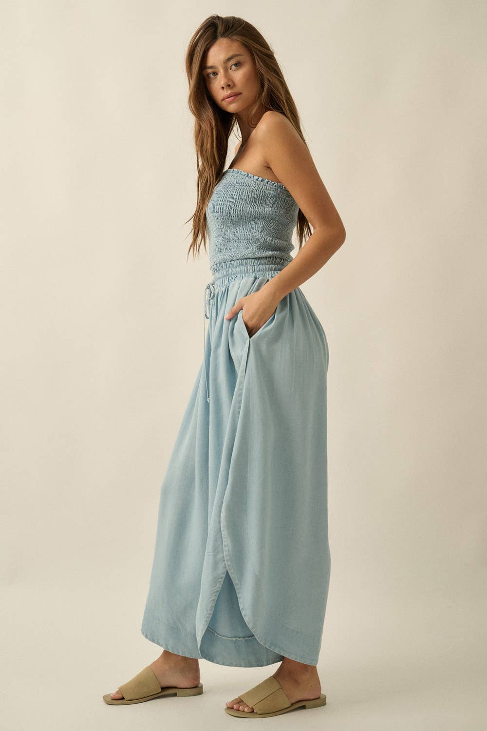 Woman wearing a light blue strapless top and wide-leg pants on a beige background