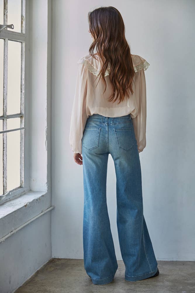 Person wearing a beige blouse and blue jeans standing in a room with a window.