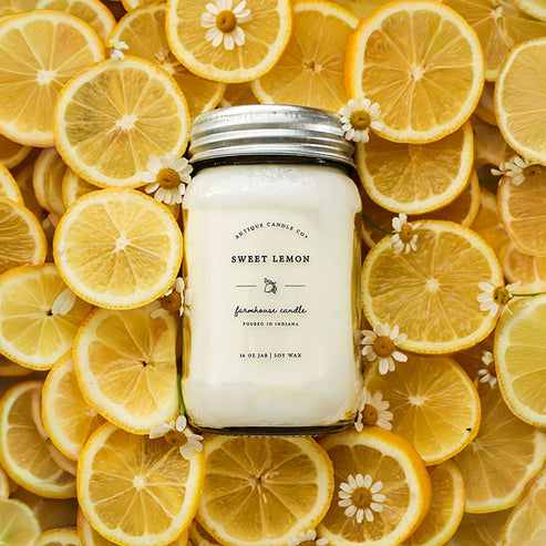 Sweet Lemon 16 oz soy candle surrounded by fresh sliced lemons and flowers for bright citrus kitchen scent.