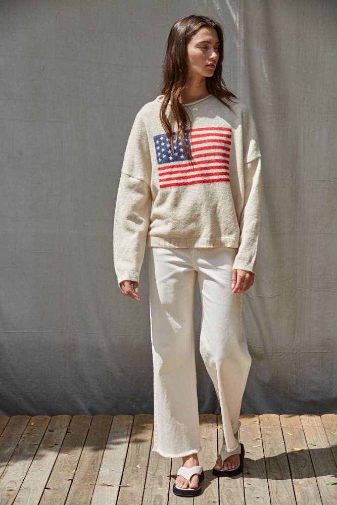Woman wearing a cream sweater with an American flag design against a gray curtain background.