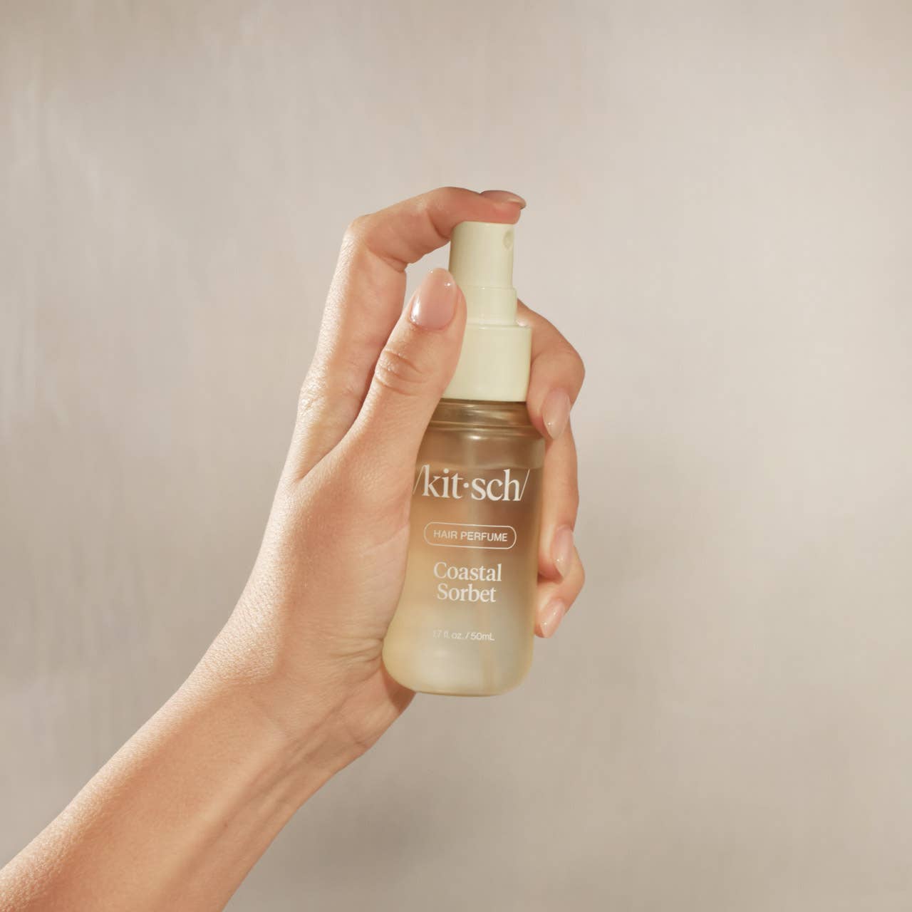 Hand holding a 'kit-sch' perfume bottle against a neutral background