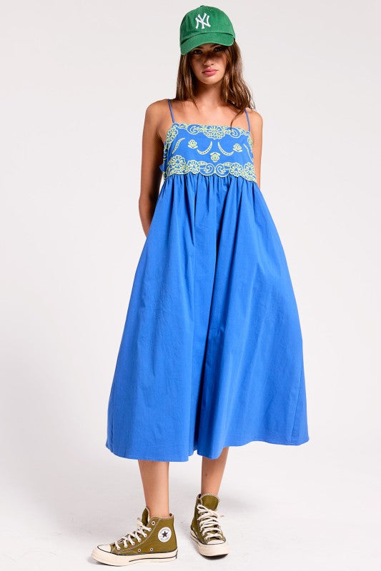 Woman wearing a blue dress with floral lace top and green cap on a white background