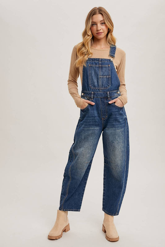 Woman wearing dark wash barrel-leg denim overalls with adjustable straps and wide-leg fit