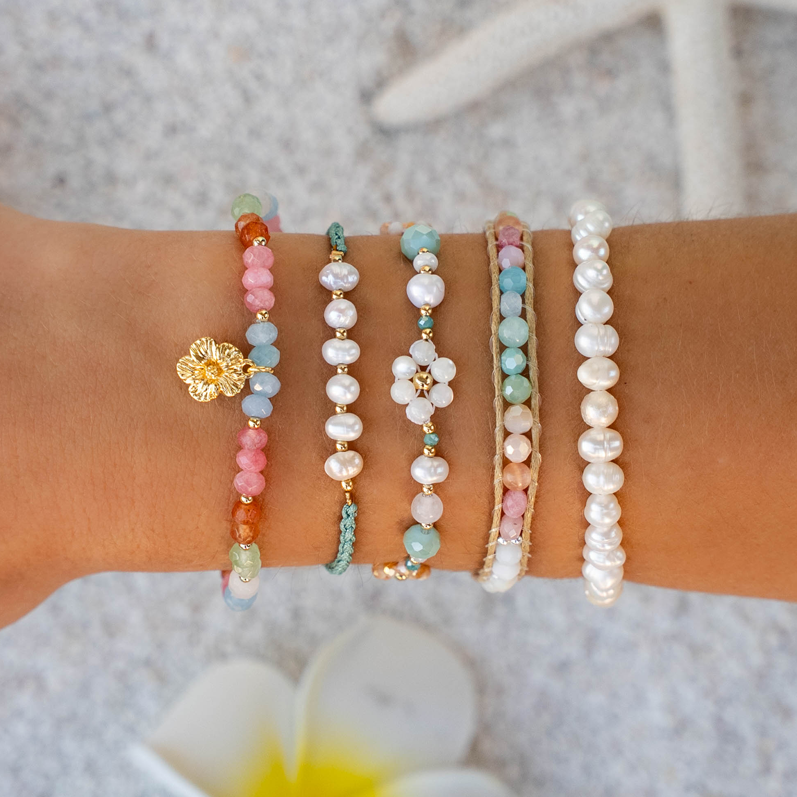 Collection of colorful beaded bracelets on a wrist with a blurred floral background